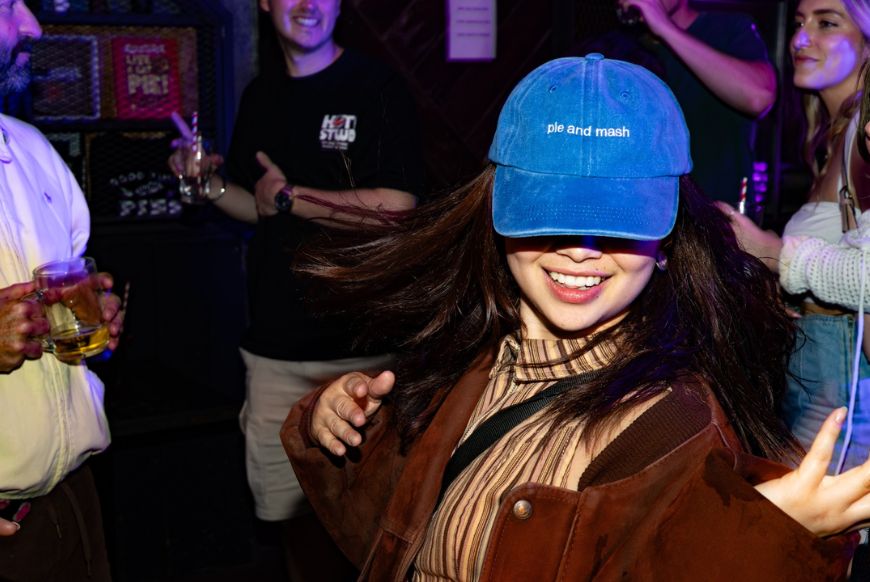 a woman dancing wearing a denim cap with the words 'pie and mash' printed on it
